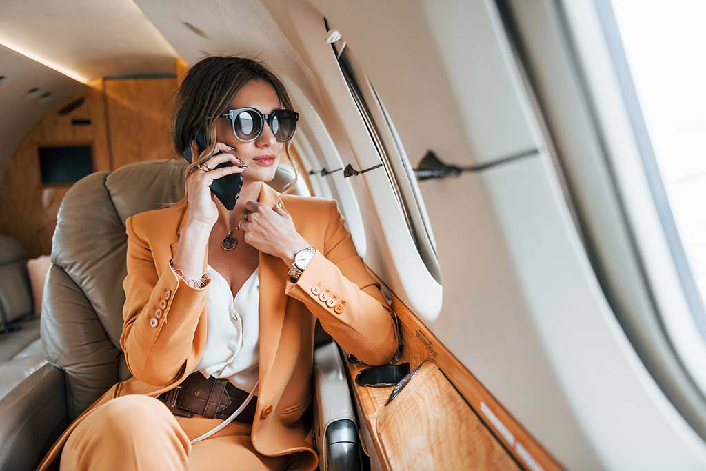 Uses phone. Young passenger woman in yellow clothes is flying in the plane.